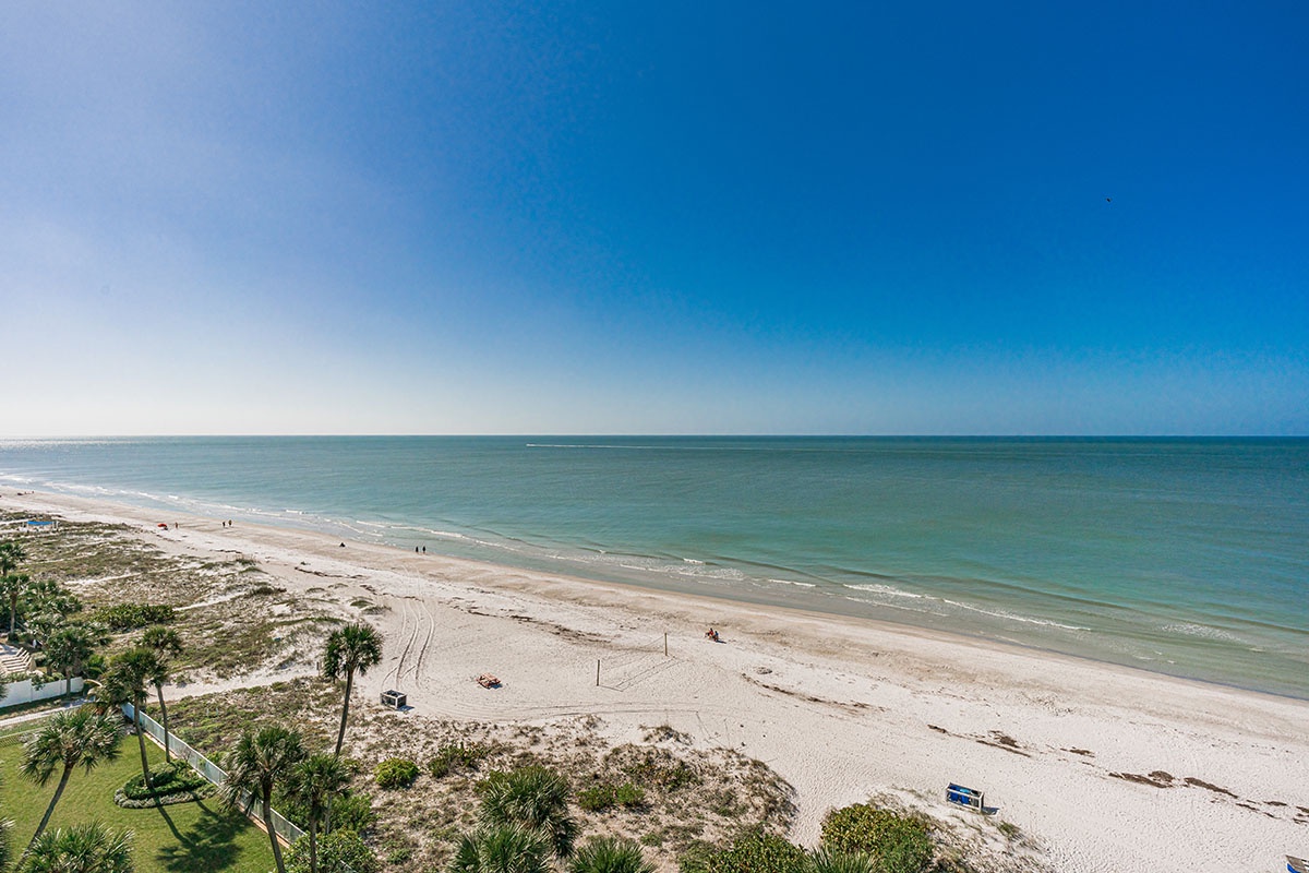 Pristine Gulf Coast beach with white sand stretches beneath brilliant blue skies, perfect for peaceful beachfront relaxation.