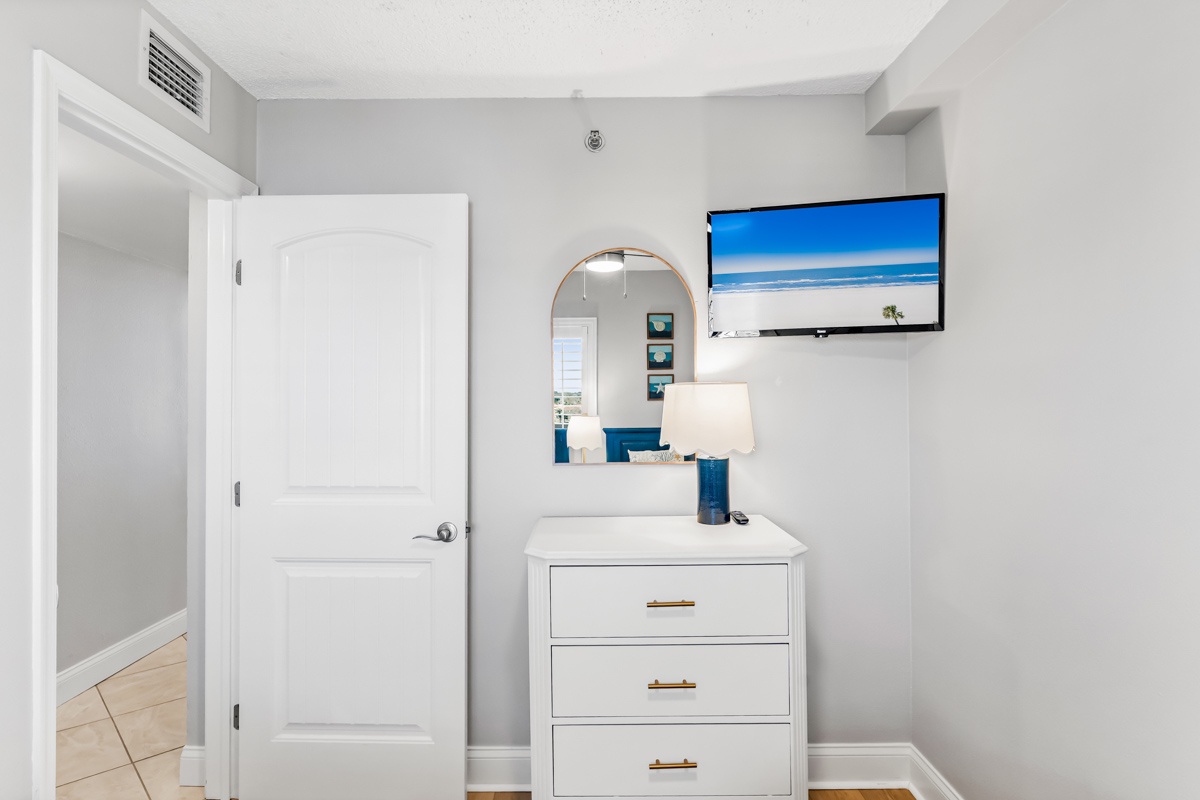 Your bright bedroom dresser area features a sleek white dresser, stylish round mirror, and wall-mounted TV for relaxing evenings.