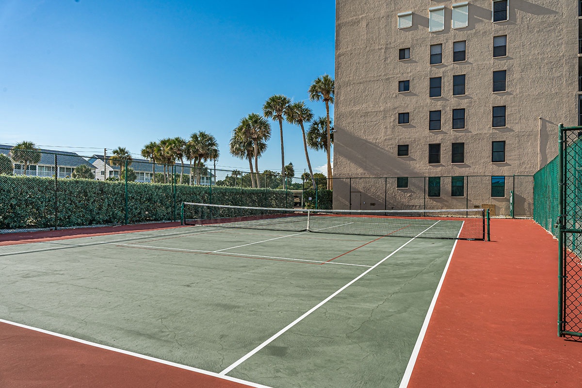Well-maintained tennis court surrounded by palm trees and adjacent property buildings offers recreational opportunities during your stay.