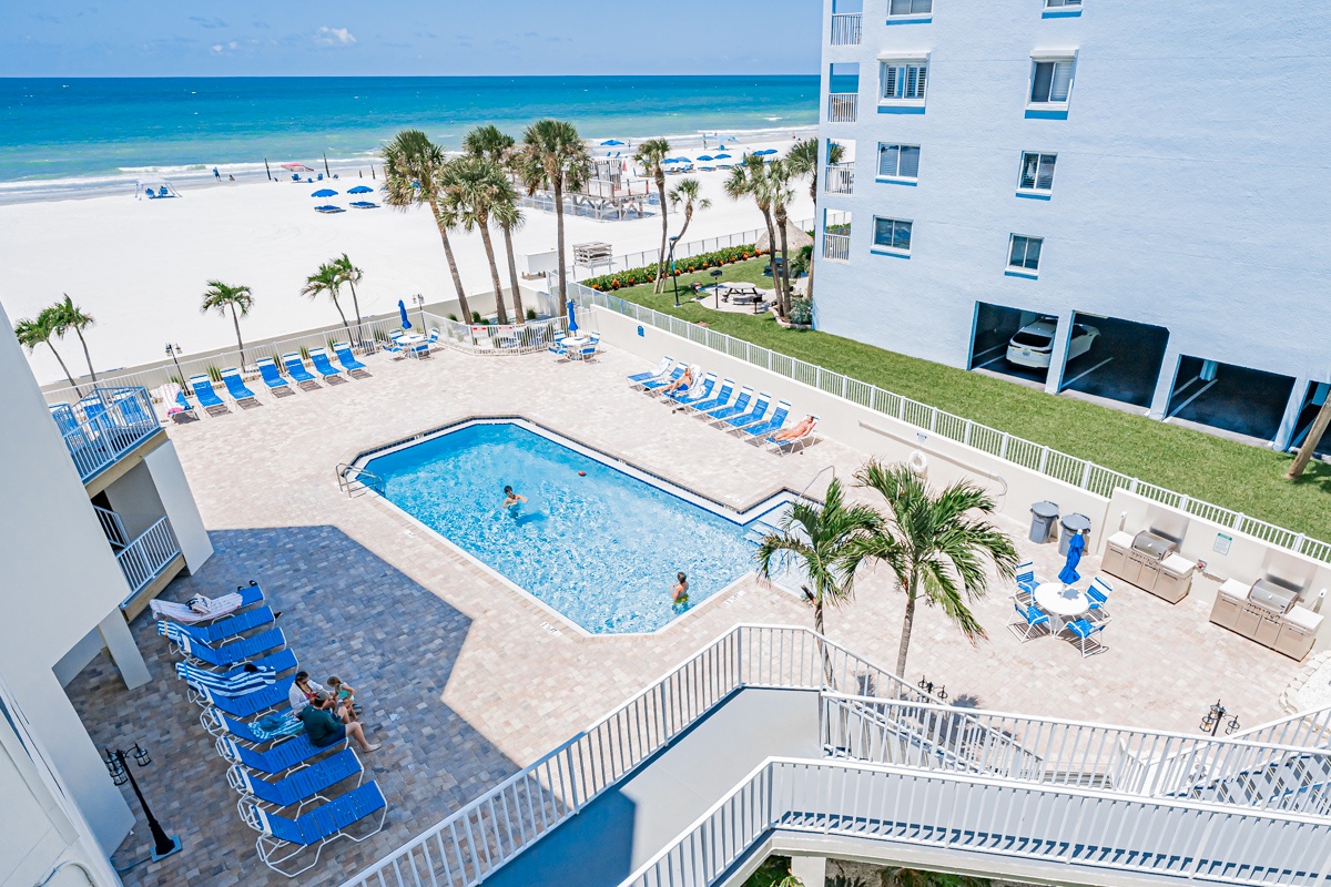 An elevated view of the pool deck and surrounding area, just steps from the beach. The sparkling blue ocean and swaying palm trees set the scene for your perfect beachfront getaway.