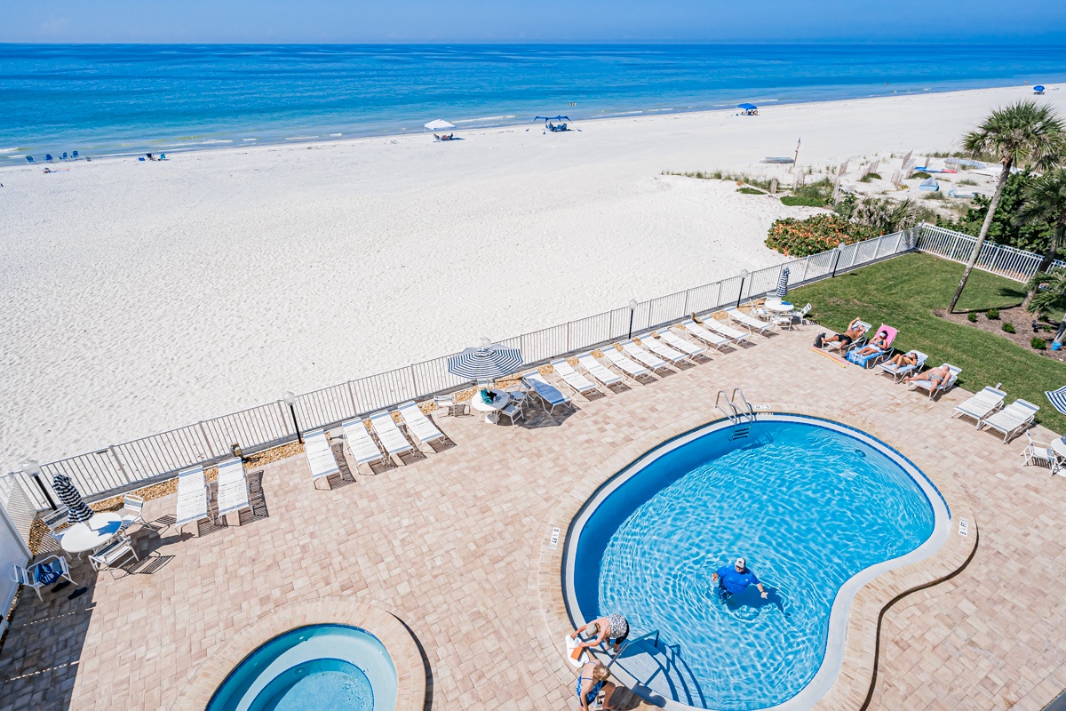 The pool area overlooks the beachfront location, with direct access to a wide stretch of white sand and turquoise Gulf waters beyond the landscaped grounds.