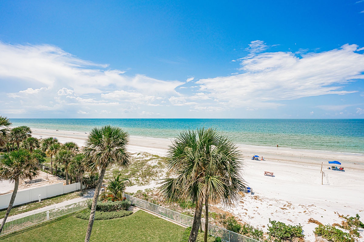Stunning beachfront location with pristine white sand and crystal-clear waters stretching to the horizon under brilliant blue skies.
