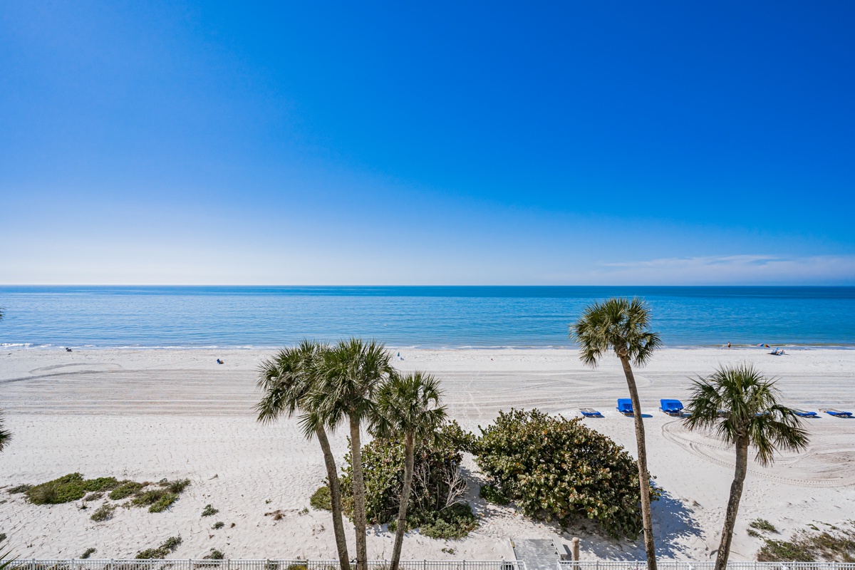 Pristine white sand beach with palm trees and azure waters stretches endlessly under brilliant blue skies.
