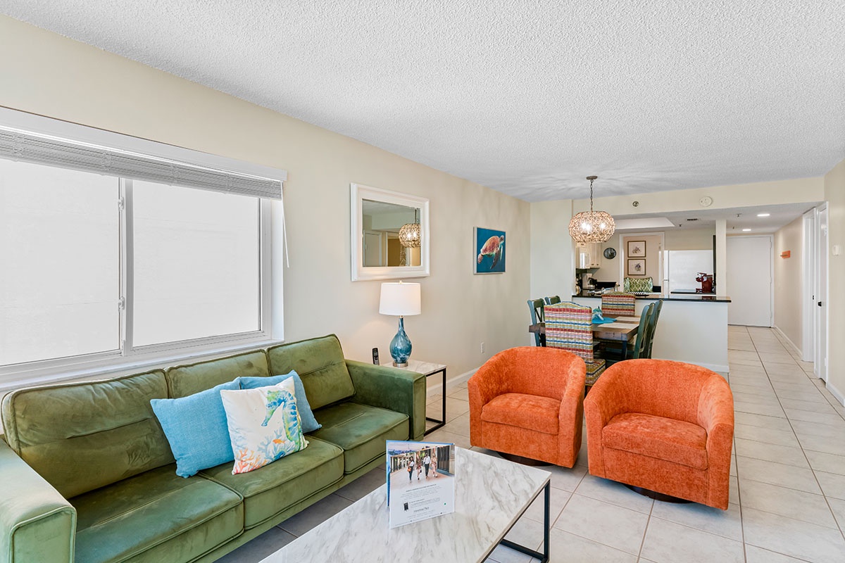 Relax in your bright, modern living space with vibrant orange chairs and cozy green sofa. The open layout flows seamlessly into your dining area.