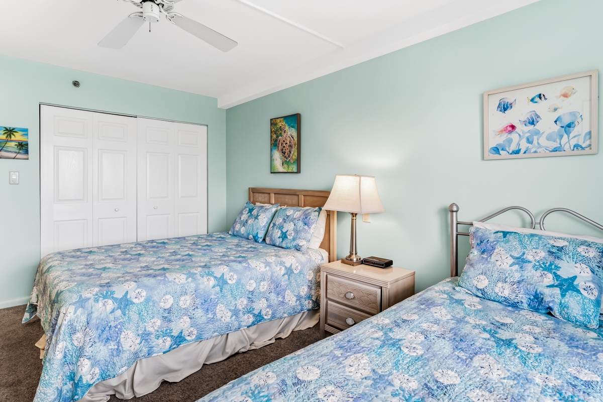 Drift off in comfort in this serene coastal retreat, with two plush beds, Queen and Twin, dressed in breezy blue linens. The soft turquoise walls and charming beach-themed art create a peaceful, seaside ambiance.