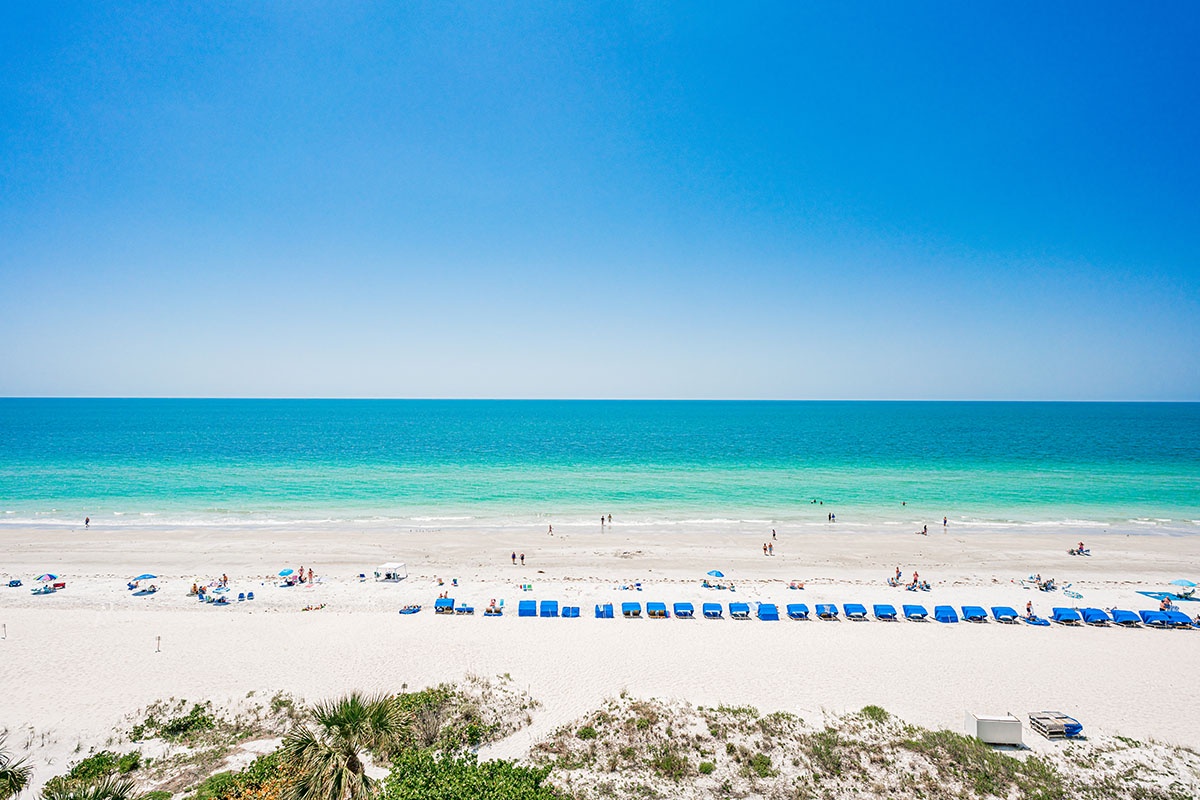 Pristine white sand beach with crystal-clear turquoise waters stretching endlessly under brilliant blue skies.