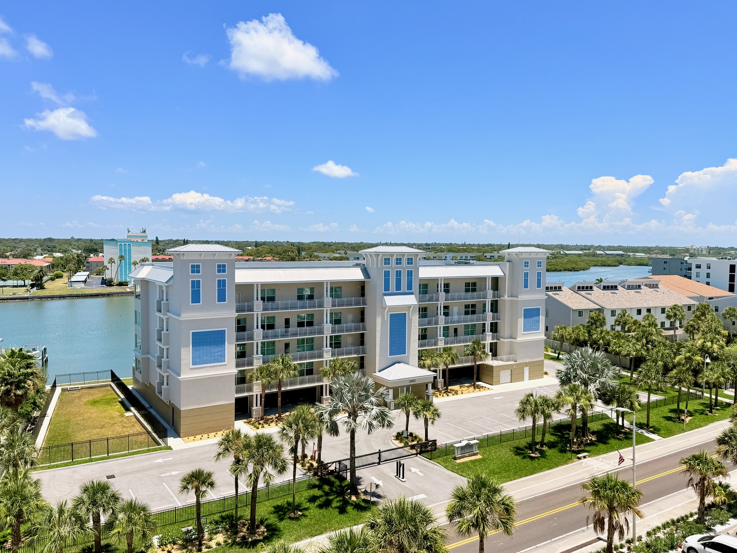 Contemporary waterfront building featuring modern architecture with striking blue and white accents, surrounded by tropical palm trees and scenic water views throughout the surrounding area.