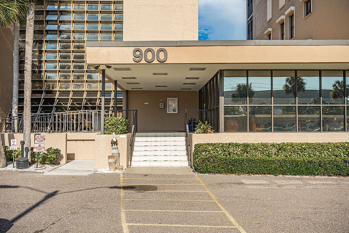 Modern apartment building entrance at 900 with convenient parking and tropical landscaping in a sunny residential area.