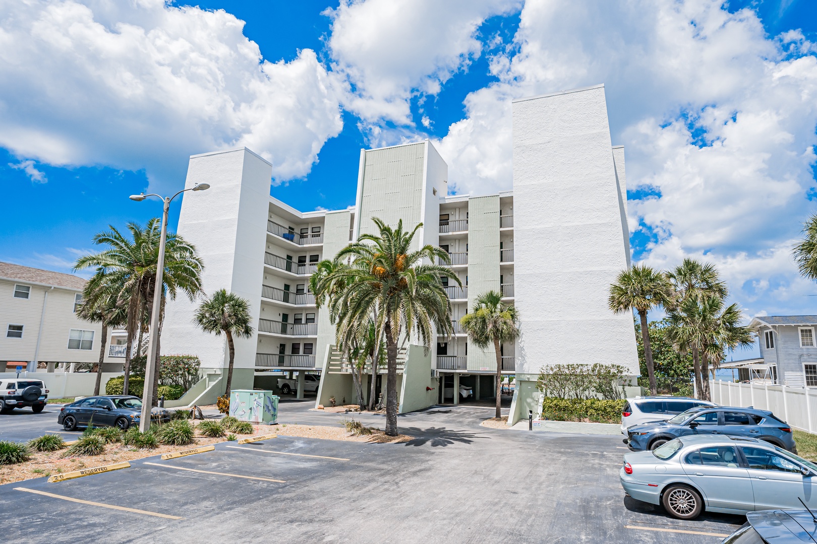 A modern white beachside building surrounded by swaying palm trees offers convenient parking and easy access to coastal living in a vibrant neighborhood.