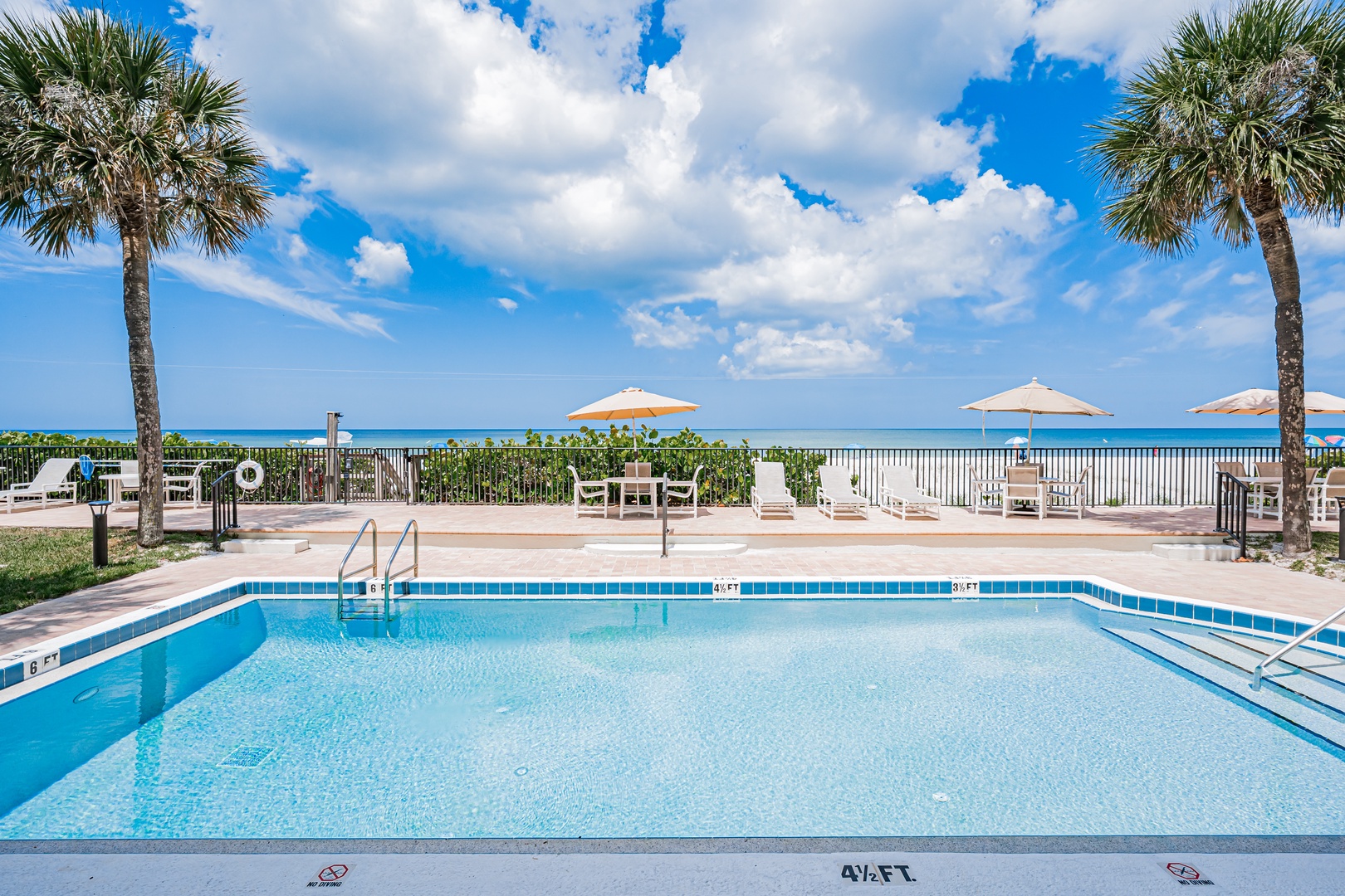 Sparkling beachfront pool framed by swaying palms, with loungers and umbrellas set against turquoise waters—your perfect tropical escape awaits.