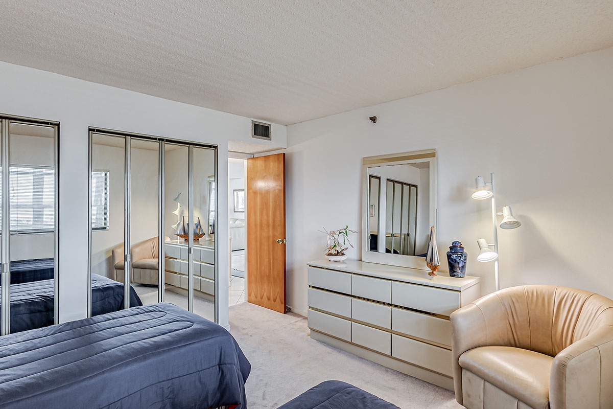 Relax in your spacious bedroom featuring mirrored wardrobes, modern furnishings, and a comfortable leather chair for reading.