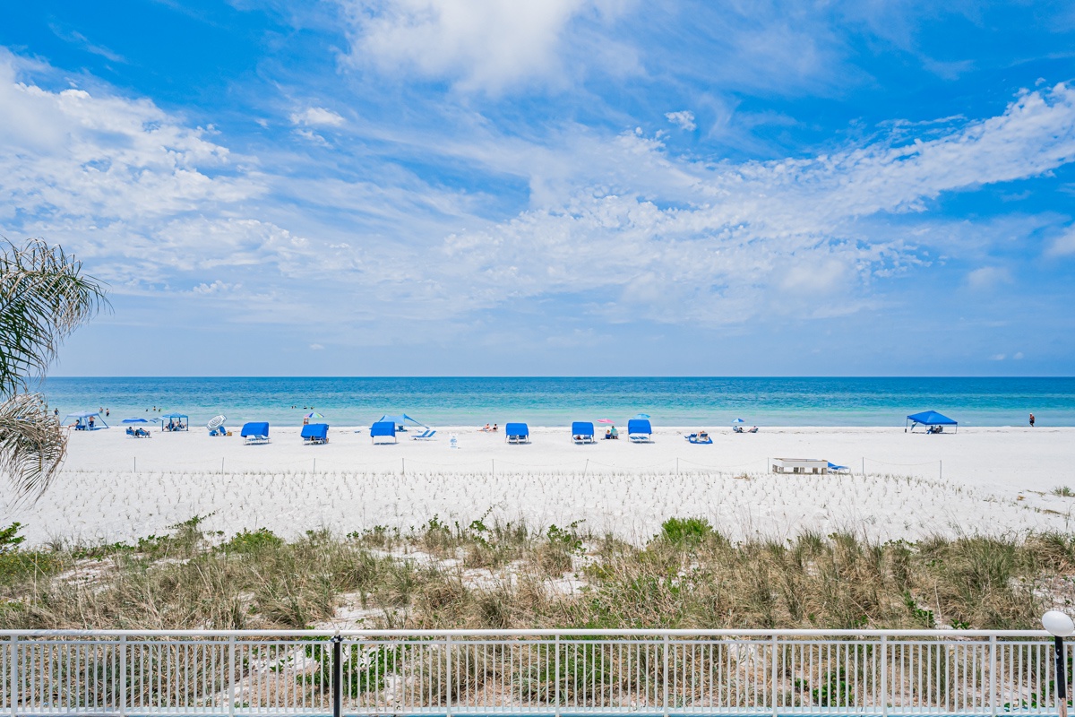 Pristine white sand beach with turquoise waters stretching to the horizon, featuring cozy blue umbrellas and lounge chairs perfect for your sunny beach day.