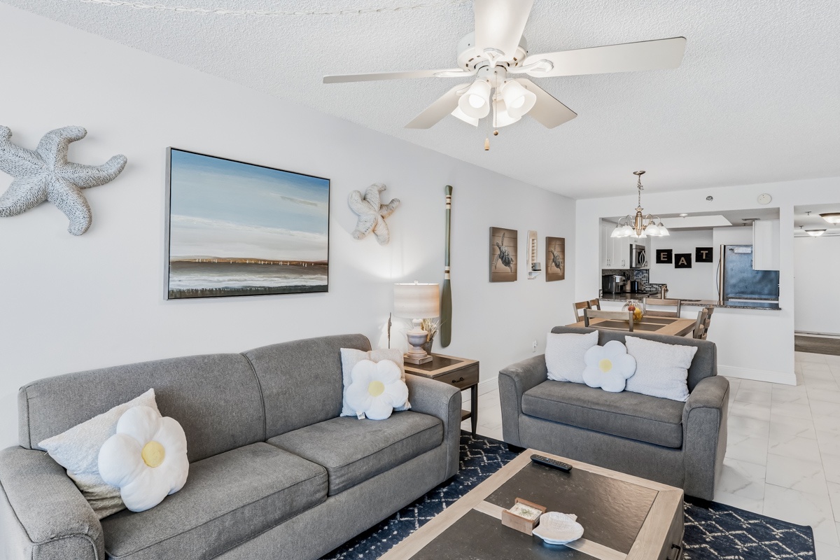 Relax in your bright open living space featuring comfortable gray sofas, coastal decor, and a ceiling fan to keep you cool during your stay.