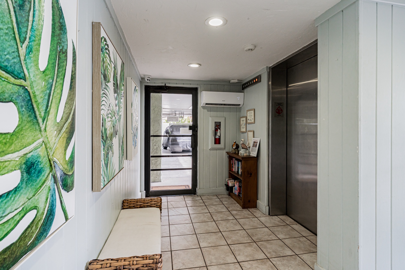 The property's modern entrance hallway features bright tropical artwork, tile flooring, and convenient elevator access for easy arrival.