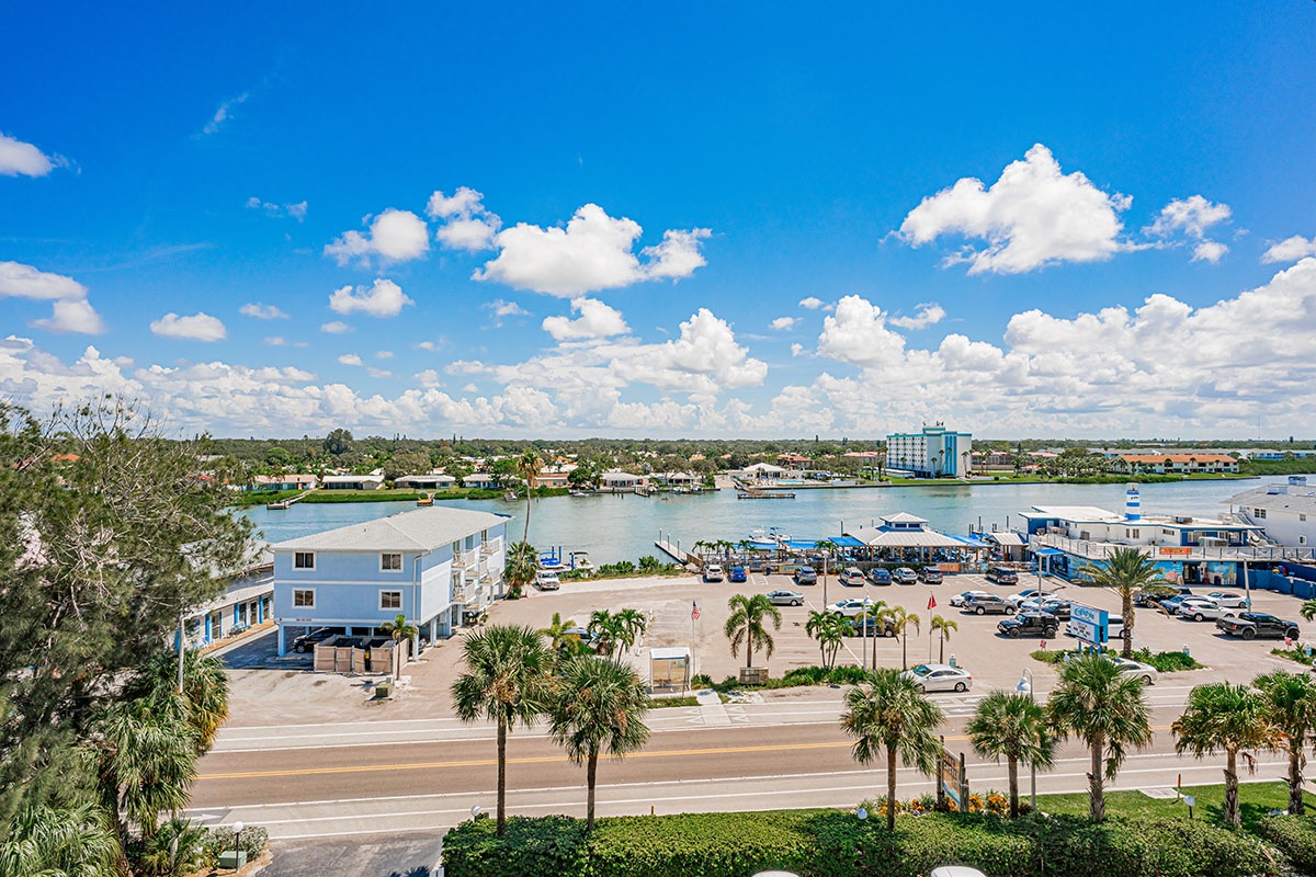 Coastal community with marina, waterfront dining, and palm-lined streets under vibrant blue skies with fluffy white clouds.