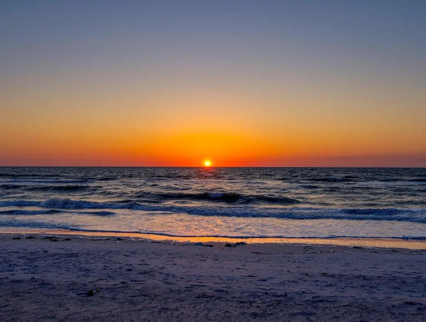 Spectacular sunset paints the sky in brilliant oranges and purples over the pristine beach waves.
