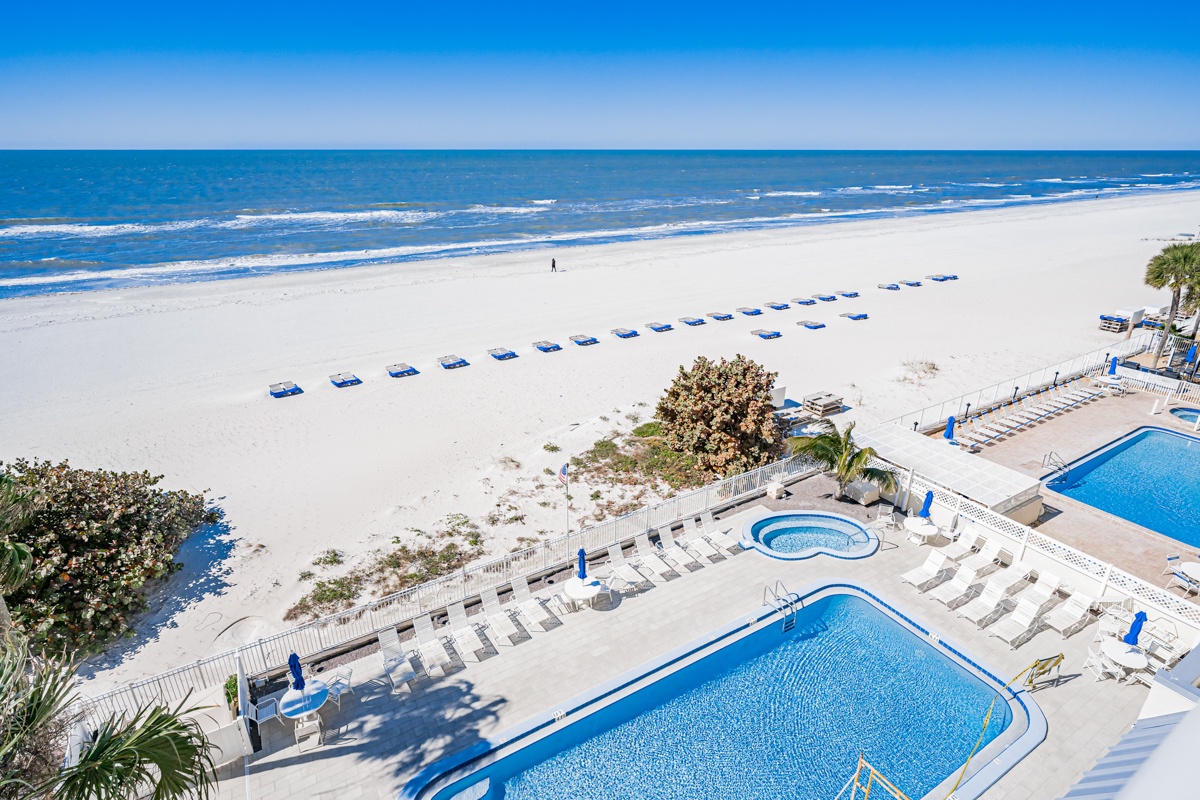 Beachfront resort featuring swimming pools, hot tub, and direct access to pristine white sand beach with blue umbrellas.