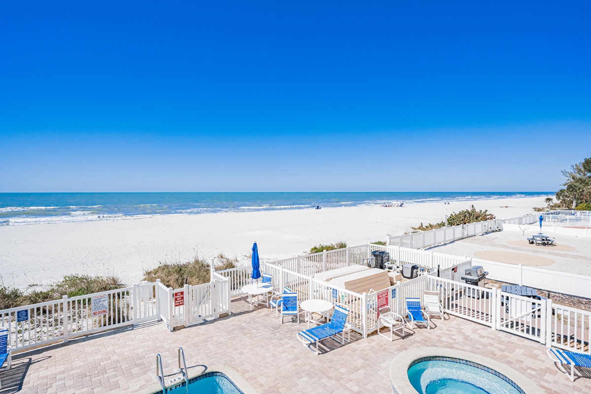 Pristine beachfront with crystal-clear waters stretches endlessly before this property's deck area featuring pool facilities and direct beach access.