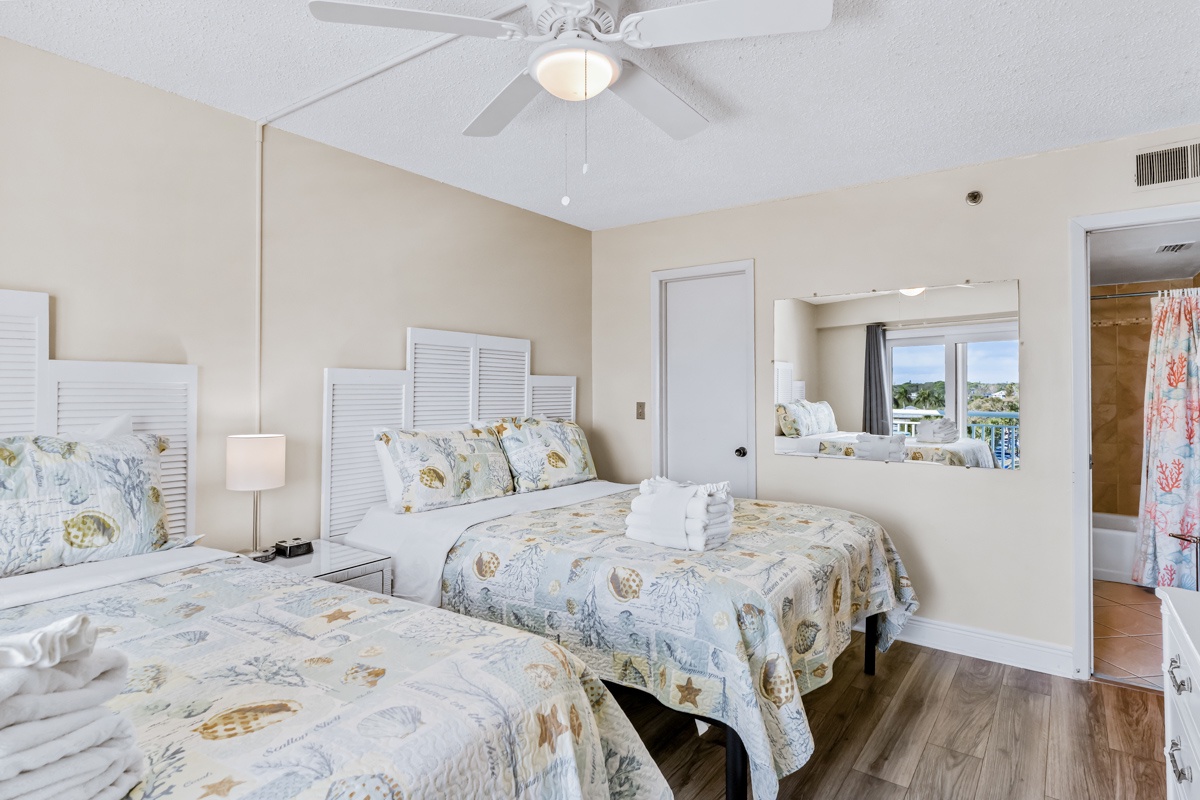Your coastal bedroom features twin beds with charming seashell linens, ceiling fan for gentle breezes, and views of the surrounding area.