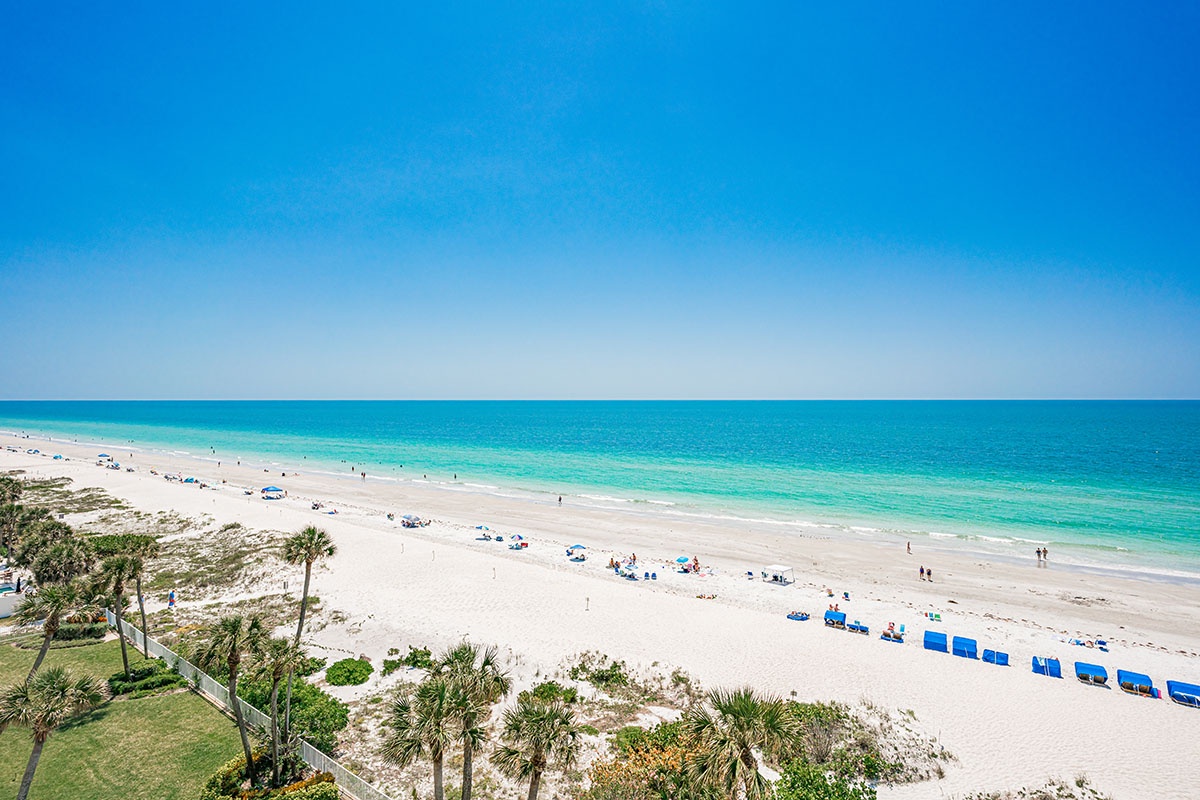 Pristine white sand beach with crystal-clear turquoise waters stretches endlessly under brilliant blue skies, offering the perfect tropical paradise setting.