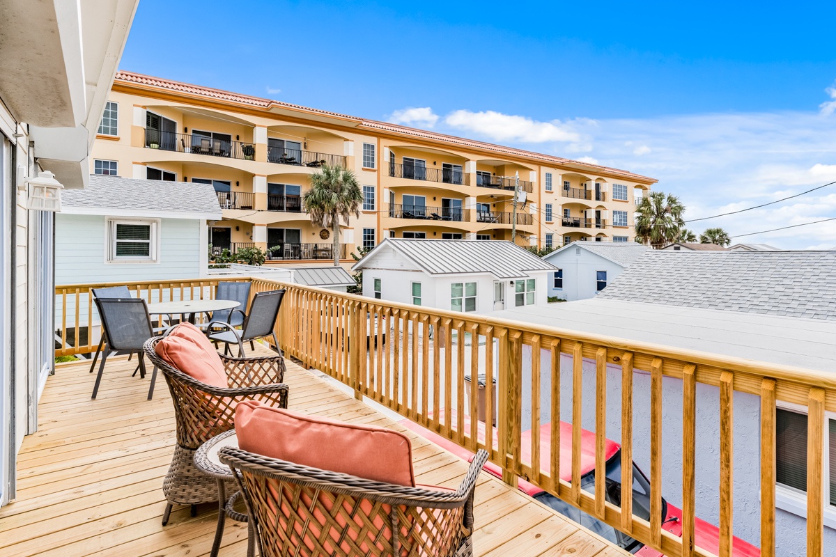 Unwind on your private deck with coral cushions and wicker seating, overlooking the coastal neighborhood on a perfect sunny day.