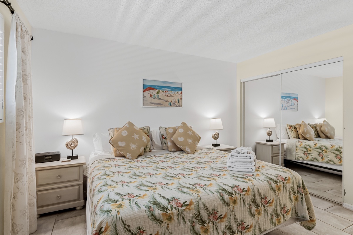 Sink into this bright, airy bedroom with its plush bedding and tropical touches. Your mornings here begin with soft light and coastal charm, inviting relaxation from the moment you wake.