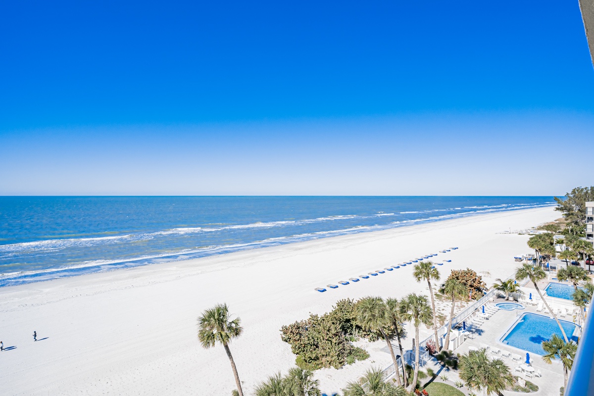 Expansive beachfront with pristine white sand stretches along turquoise waters, complemented by tropical palms and a sparkling pool area.