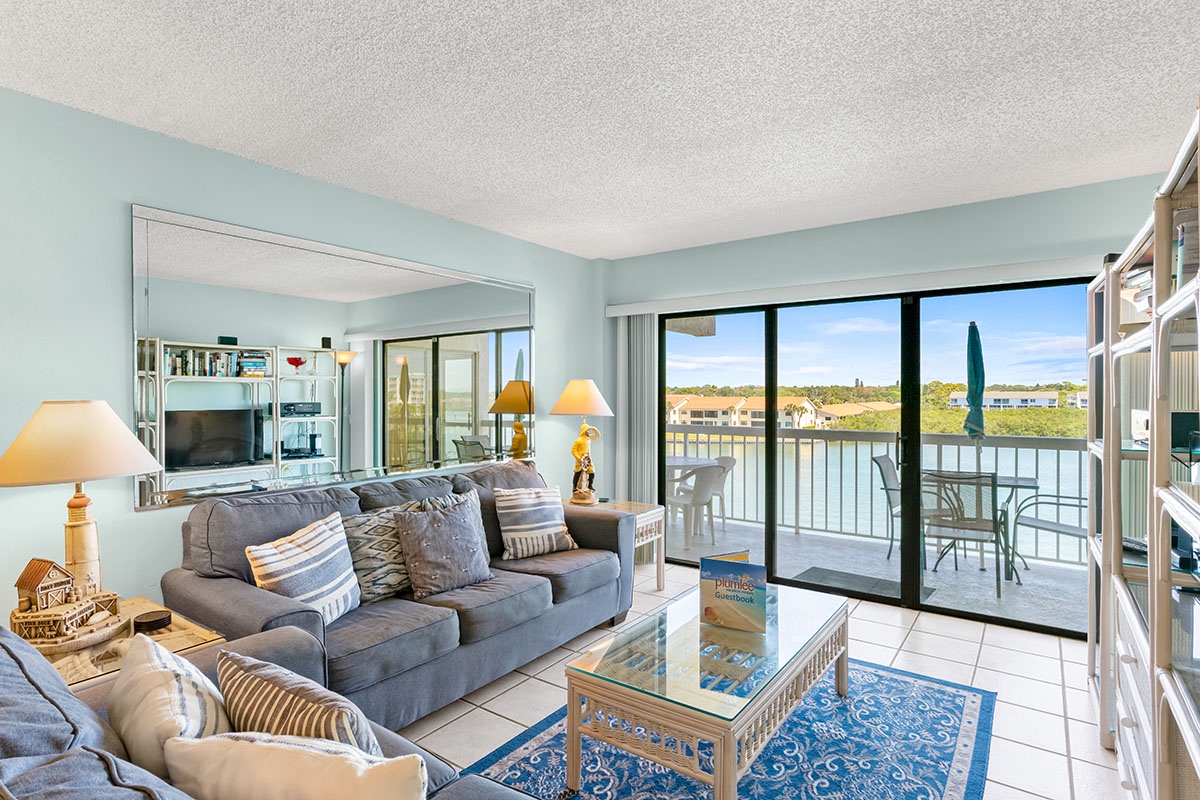 Settle into your bright waterfront living room where soft blue walls and comfortable seating create the perfect retreat for morning coffee or evening relaxation.