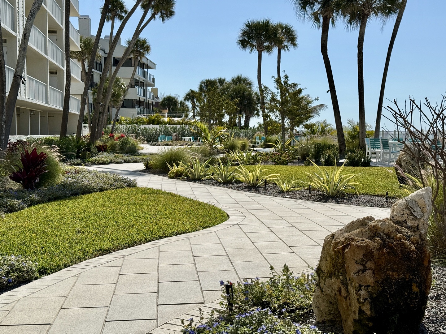 Tropical landscaping with winding pathways leads through lush gardens dotted with swaying palms.