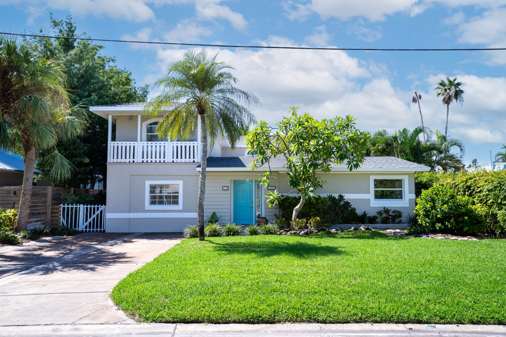 Charming coastal cottage with tropical landscaping, blue door, and front balcony creates perfect vacation retreat ambiance.