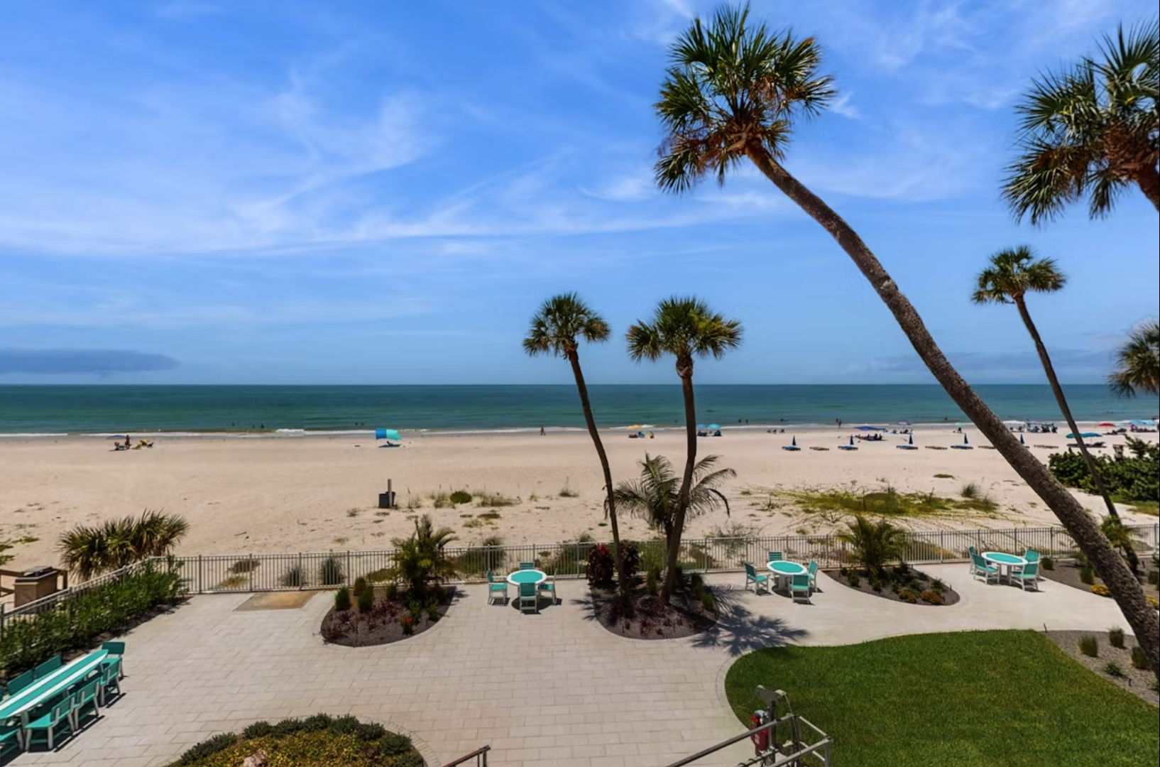 Beachfront property featuring direct access to pristine sandy shores, swaying palms, turquoise seating areas, and manicured tropical landscaping overlooking calm coastal waters.