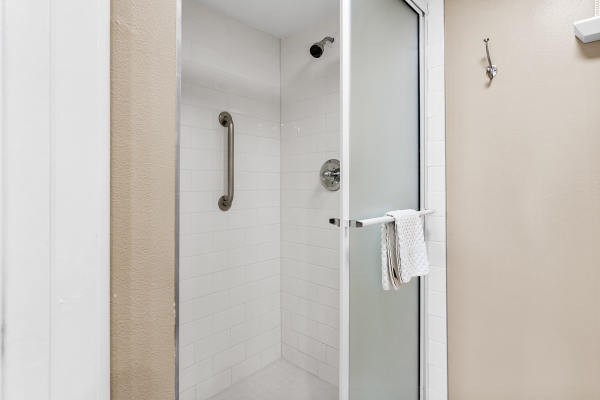 Step into your spacious glass-enclosed shower with modern fixtures and safety grab bars for a refreshing start to your day.
