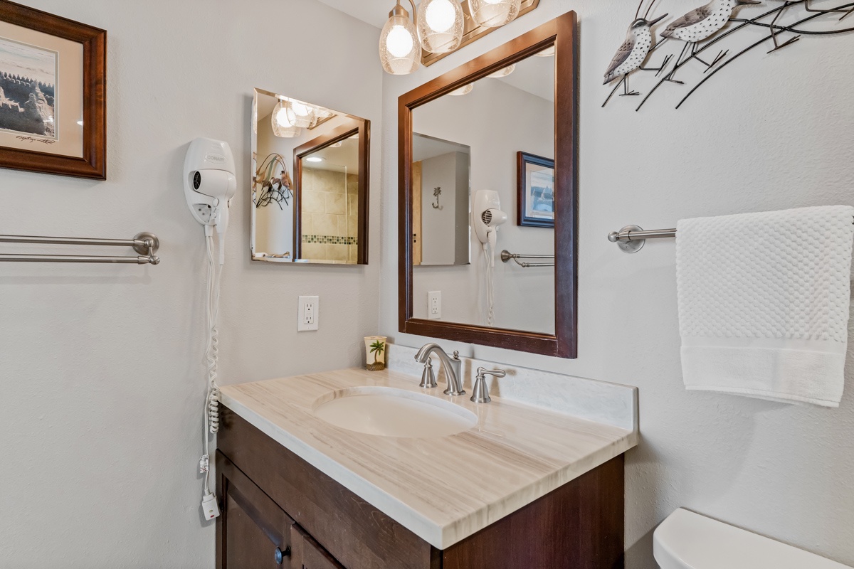 Step into your elegantly appointed bathroom featuring warm wood vanity, modern fixtures, and thoughtful amenities like a hair dryer for your convenience.