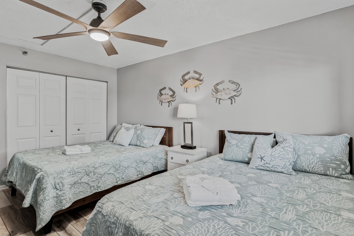 Unwind in your 2 Queen bed coastal-inspired bedroom, where ceiling fans keep you comfortable and charming nautical accents remind you of nearby shores—your peaceful retreat after a day of beachside adventures.
