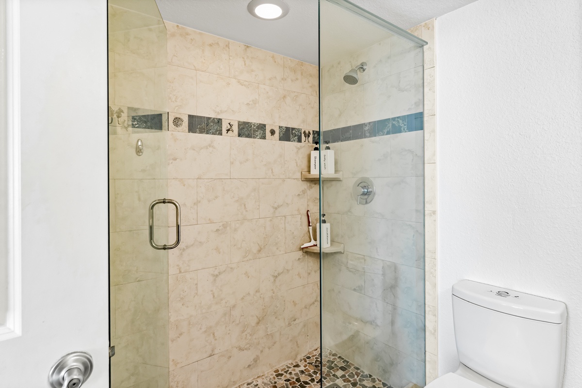 Step into your spacious glass shower with beautiful marble tiles and decorative accents - your personal spa awaits.