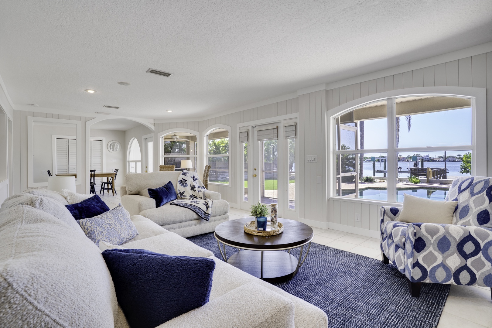 Relax in this elegant living space with coastal blue accents and stunning waterfront views through arched windows.