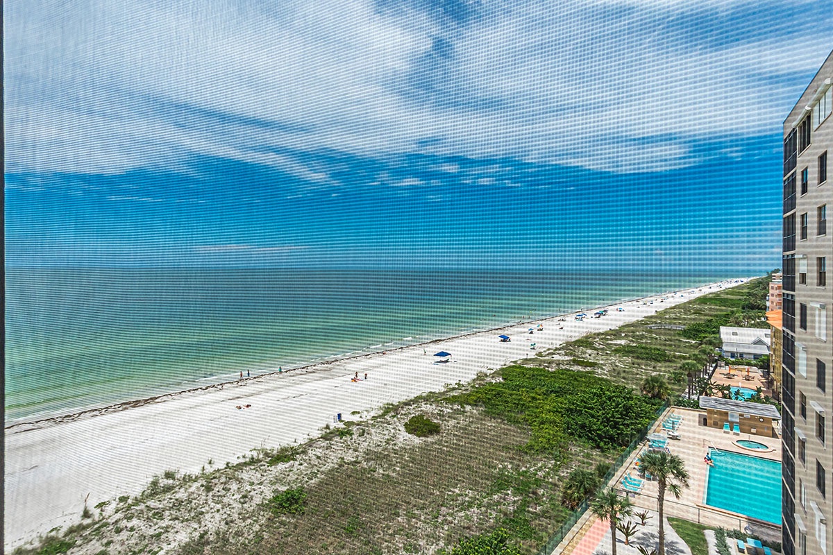 Elevated beachfront view showcasing pristine white sand beach, turquoise Gulf waters, and resort pool deck below.