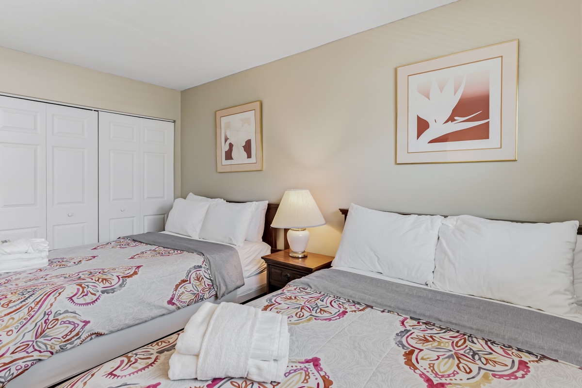 Two comfortable beds dressed in soft white linens and colorful accent bedding welcome you after a day of exploring. Warm lighting and cheerful artwork create a restful haven for your stay.