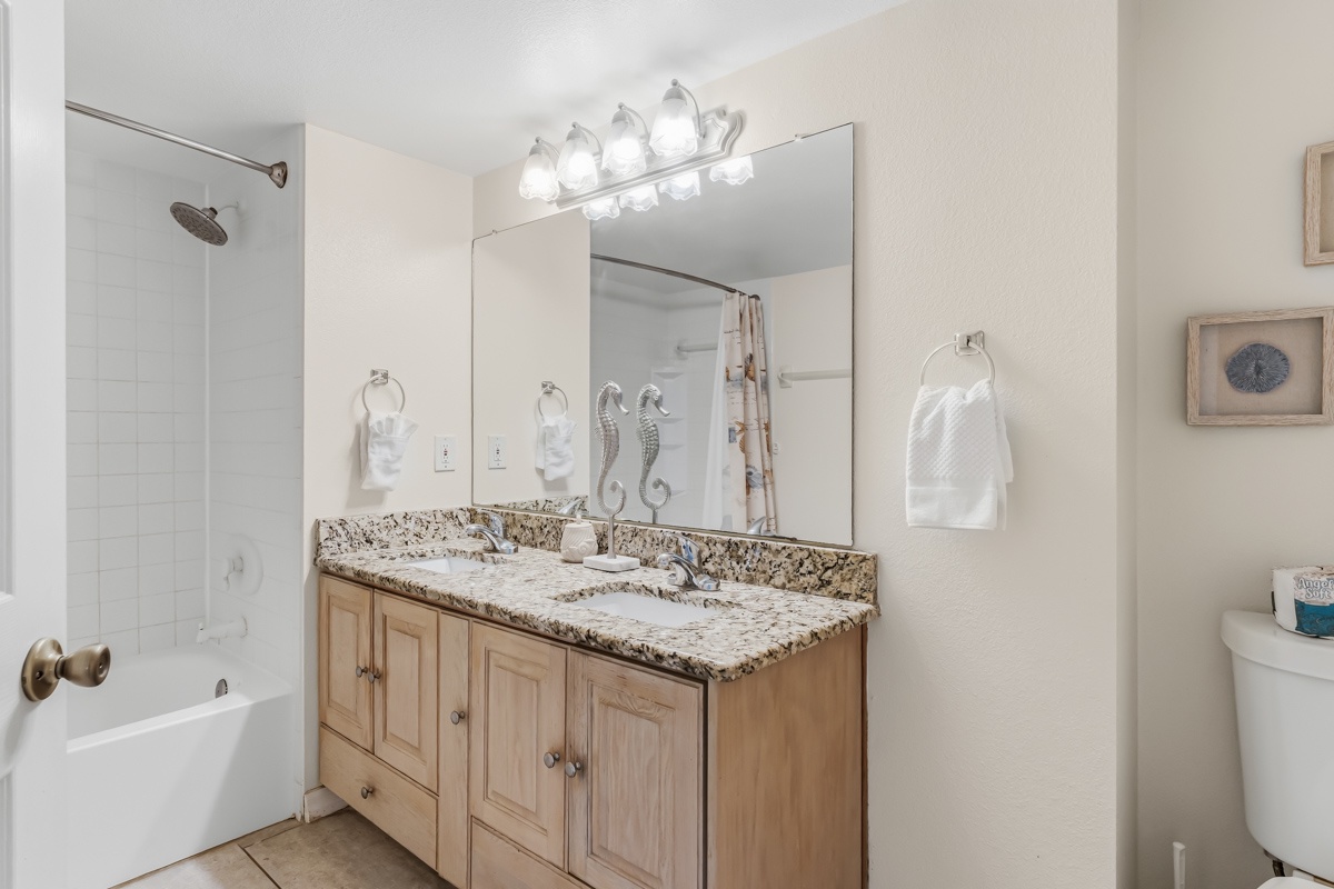 Step into your fresh, bright bathroom featuring a granite-topped double vanity, walk-in shower, and coastal-inspired décor that makes every morning feel like a breeze.