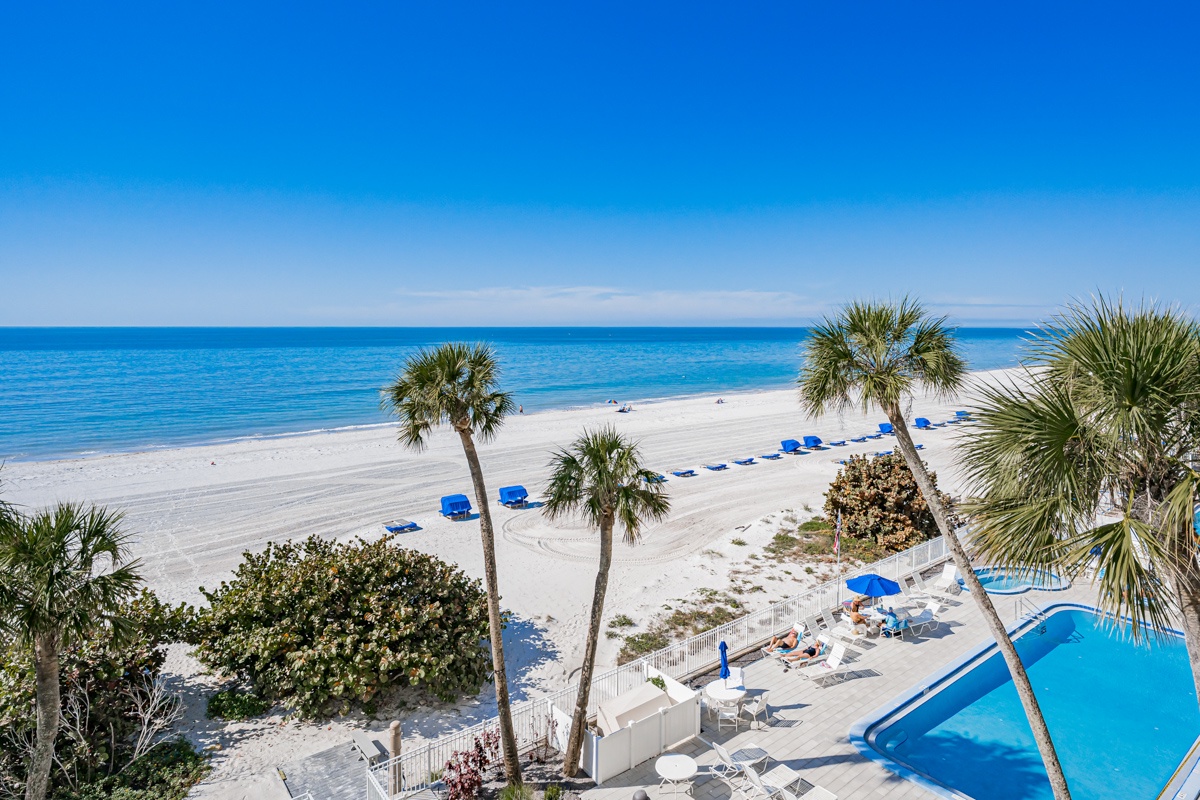 Pristine beachfront setting with crystal-clear waters, white sand, palm trees, and sparkling pool creating the perfect coastal retreat.