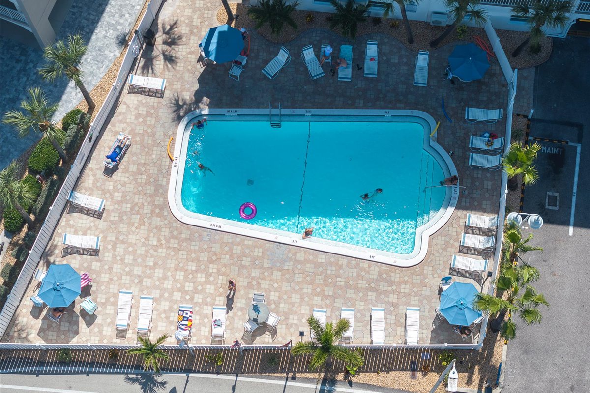 This aerial view captures the inviting swimming pool surrounded by lounge chairs, tropical palm trees, and a spacious deck—perfect for soaking up sunny days at this vacation property.