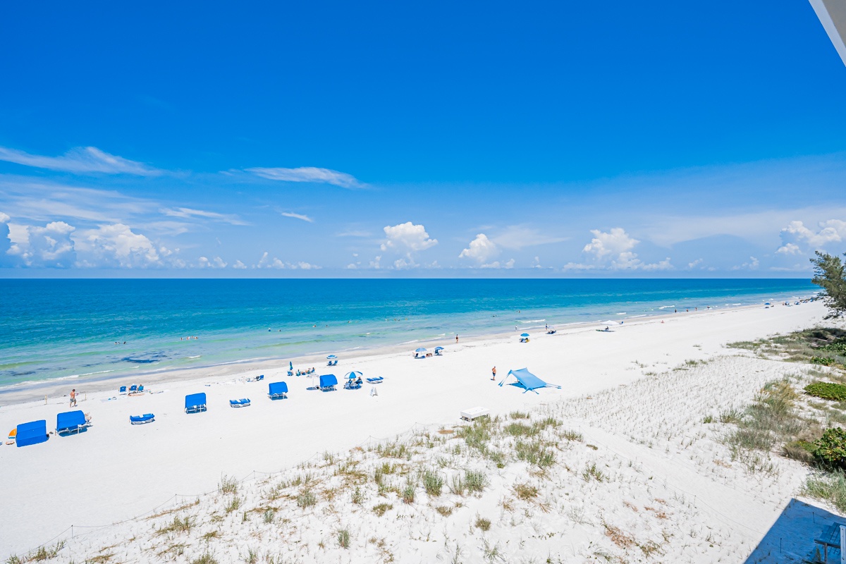 A stunning stretch of pristine white sand meets turquoise waters under brilliant blue skies, with beachgoers enjoying the sun and surf. This beautiful Gulf Coast shoreline is part of the surrounding area where your vacation retreat awaits.