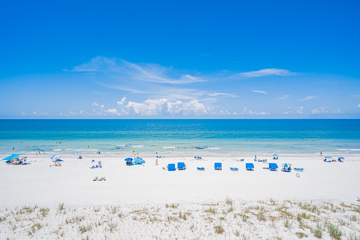 Pristine white sand stretches along turquoise waters where gentle waves invite relaxation. The beach offers plenty of space to unwind, with bright blue chairs waiting for your arrival and the soft sound of the ocean just steps away.