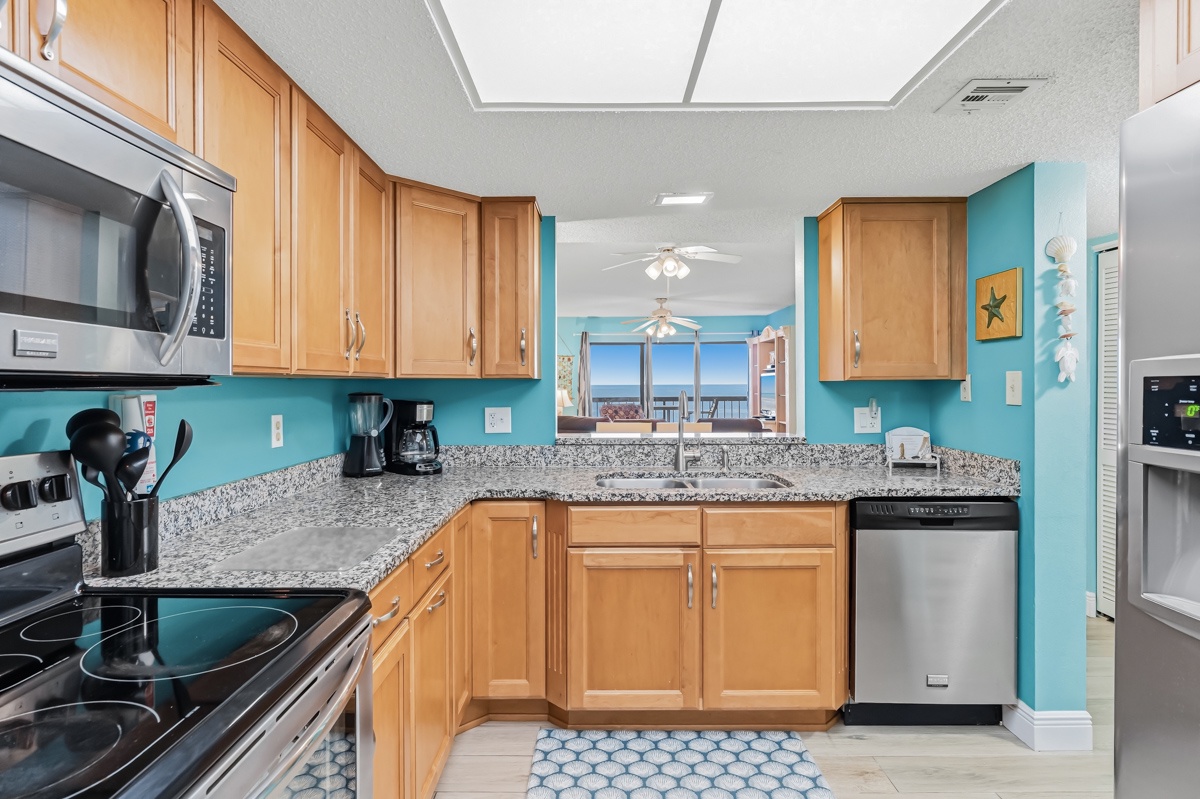 Your fully equipped kitchen invites you to prepare fresh meals with ocean views just beyond, featuring granite counters, sleek appliances, and cheerful coastal tones that make cooking feel like a vacation treat.