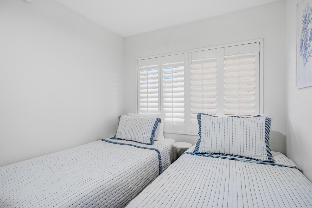 Sink into crisp white linens with charming blue accents in this peaceful twin bedroom, where plantation shutters filter gentle light for restful nights.