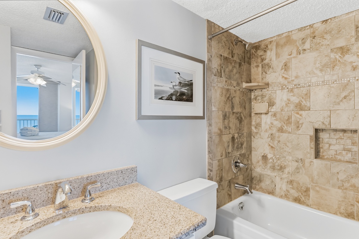 Unwind in this elegant bathroom with granite counters, marble tile shower, and calming ocean views reflected in the mirror.