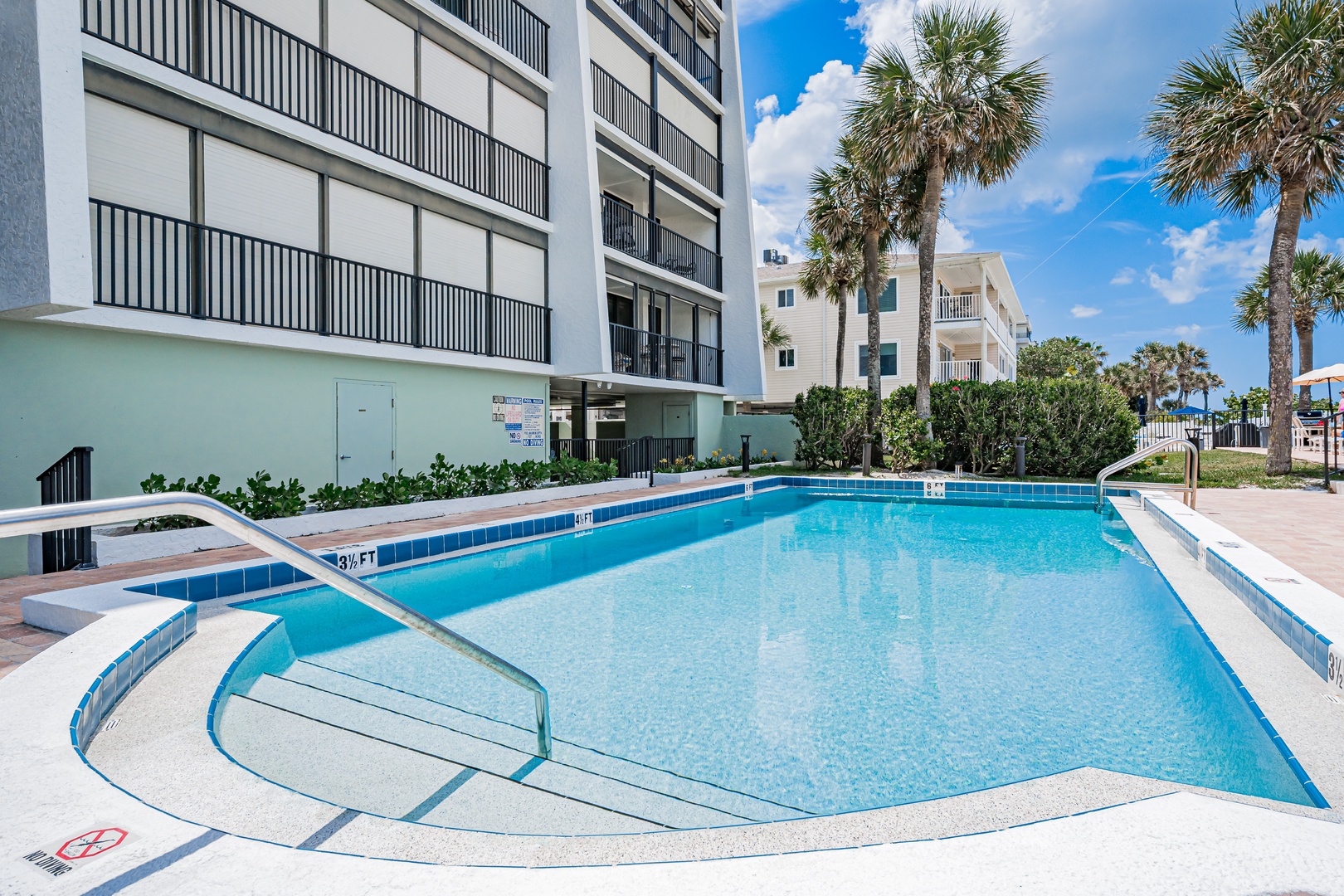 A sparkling outdoor pool surrounded by palm trees and modern condos, perfect for cooling off under the Florida sun and enjoying leisurely afternoons in the heart of your vacation retreat.