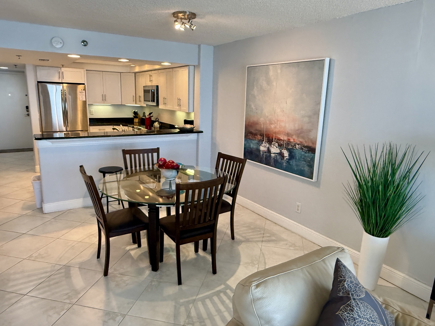 Your open-concept space flows seamlessly from kitchen to dining, where you'll share meals at the elegant glass table beneath contemporary art.