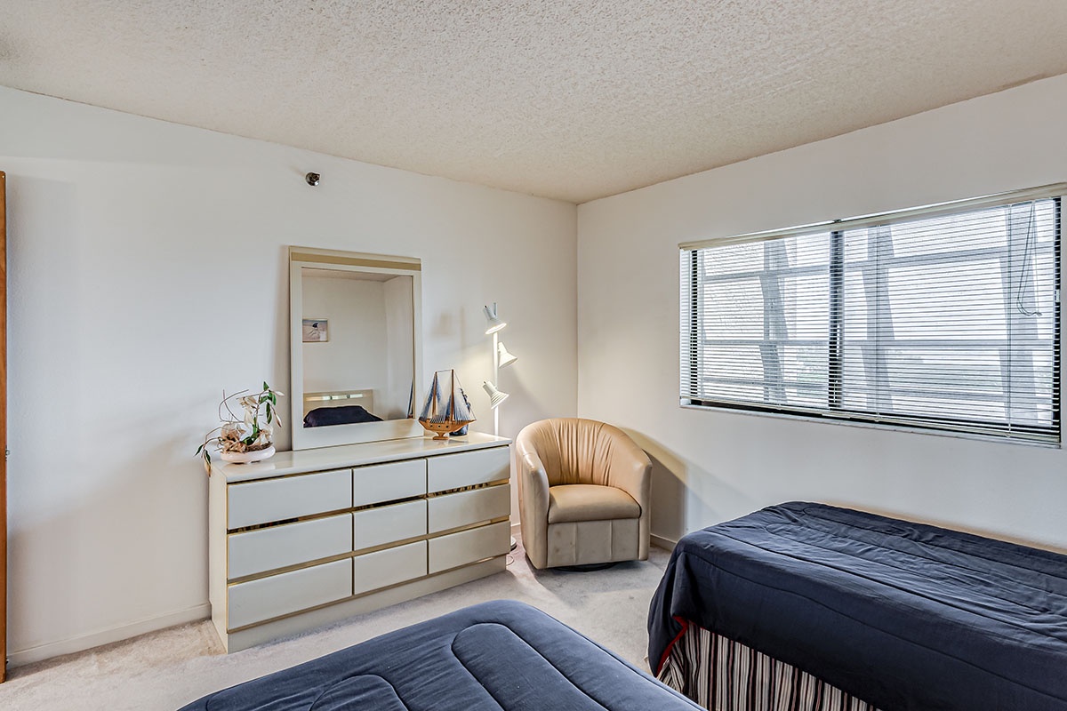 Relax in your comfortable bedroom featuring twin beds, dresser with mirror, cozy seating, and bright city views from your window.