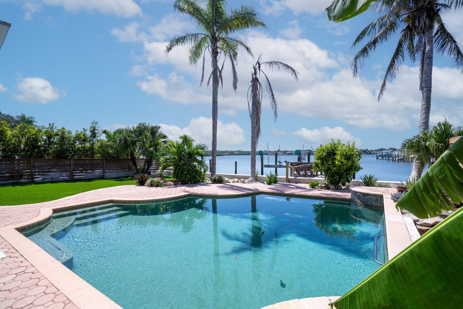 Tropical paradise awaits with crystal-clear pool overlooking serene waterfront, framed by swaying palms and lush landscaping.
